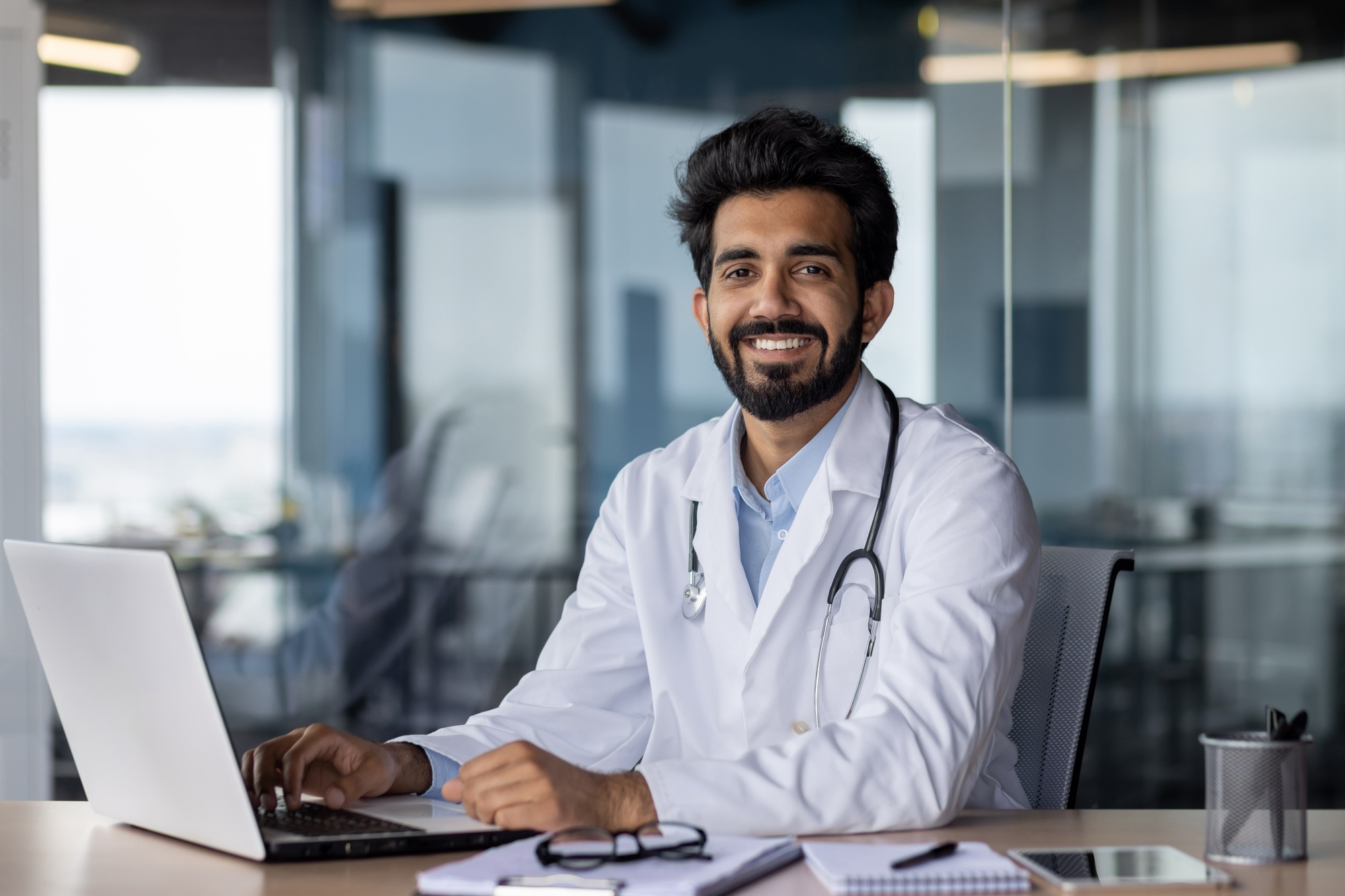 Portrait of a young doctor of Indian origin working in the office using a laptop, sitting at the